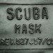 Detail štítku s názvem a zřejmě výrobním číslem masky.